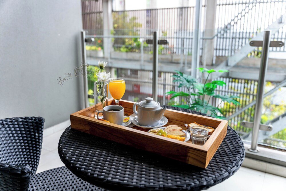 Bandeja de desayuno con tetera, jugo y tostadas sobre una mesa de mimbre