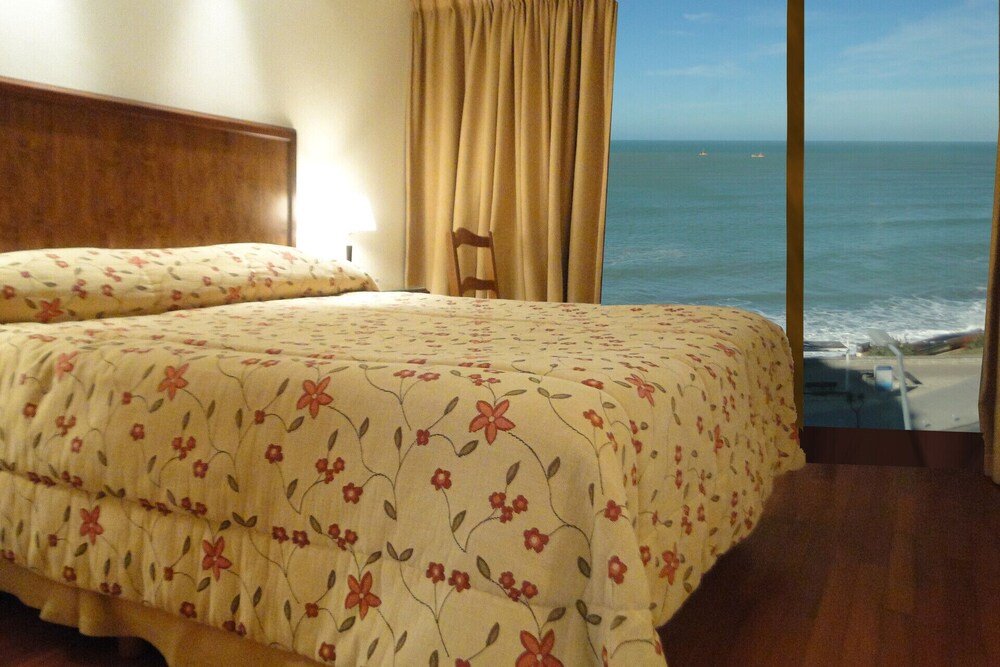 Dormitorio con cama, cabecera de madera, cortinas y vista al océano