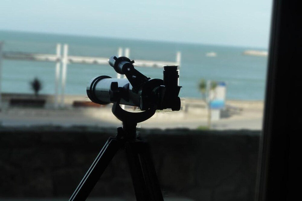 Telescopio sobre un trípode con vista a la costa, el muelle y el mar