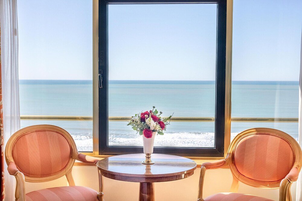 Habitación con ventanal sobre el mar, dos sillones y mesa con flores