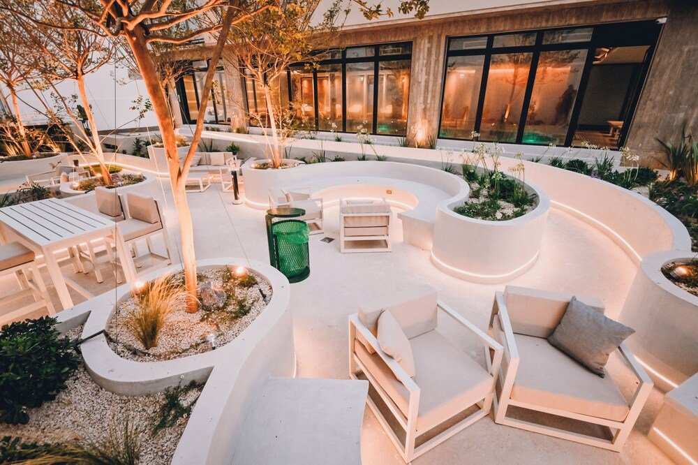 Sector exterior con muebles blancos modernos, canteros y árboles