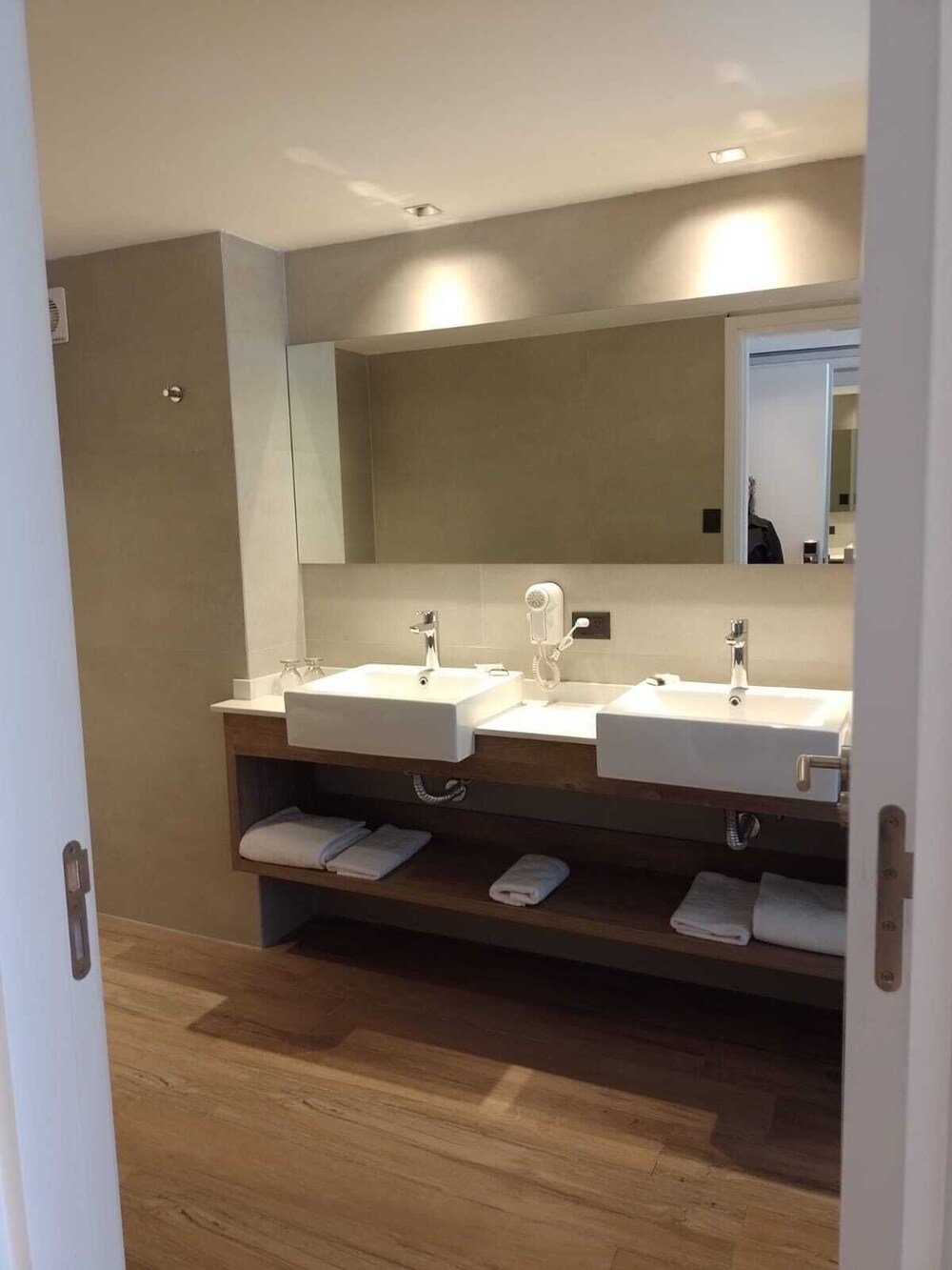 Baño moderno con dos bachas, espejo grande y piso de madera