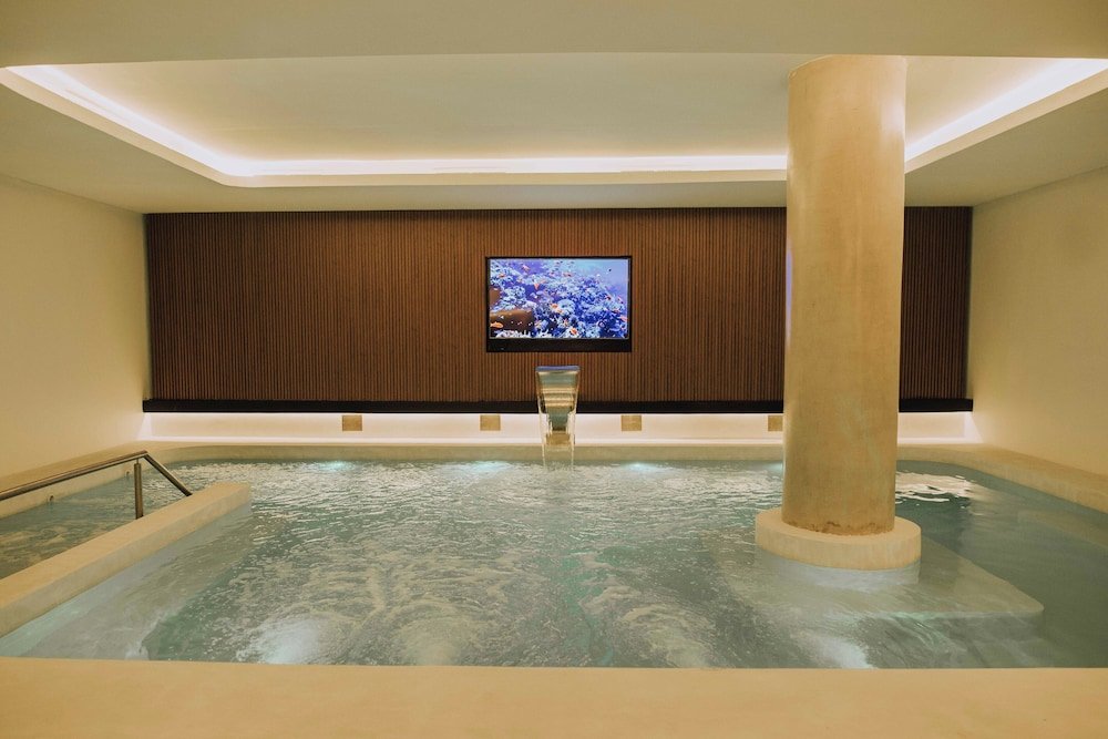 Sector de spa con jacuzzi grande, paneles de madera y televisor