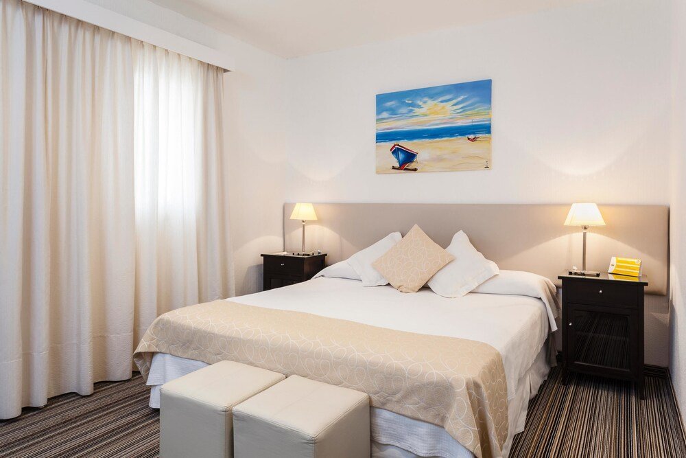 Habitación con cama grande, mesas de luz con lámparas y banqueta