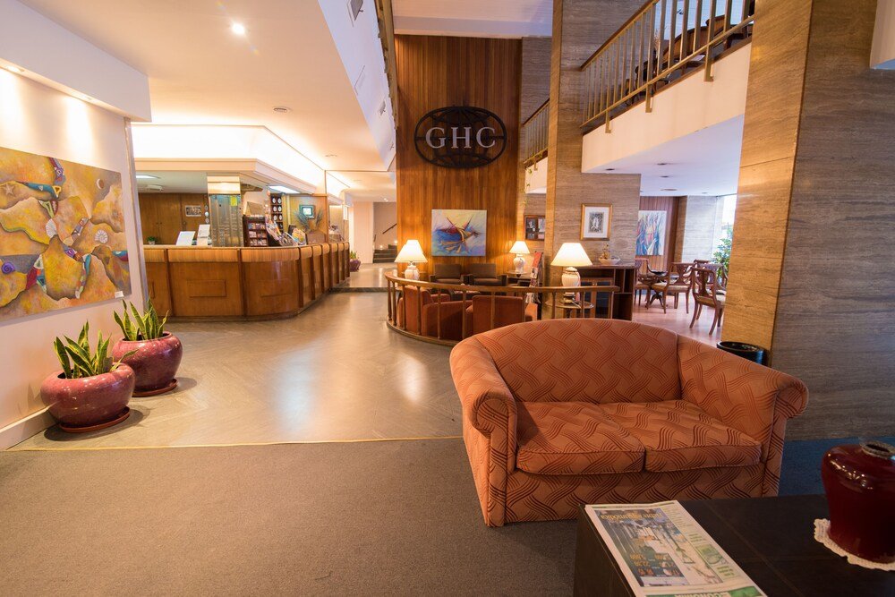 Hall del hotel con mostrador de recepción, sillón, plantas y escalera