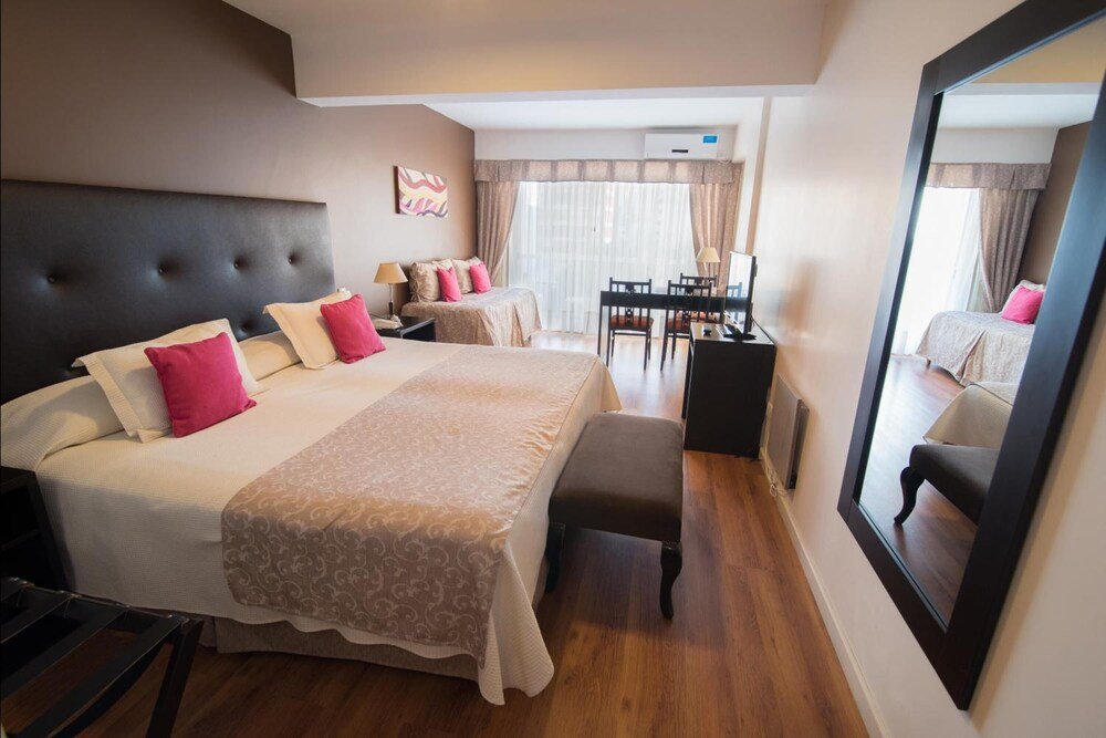 Habitación con cama grande, escritorio, silla, espejo y ventana con cortinas