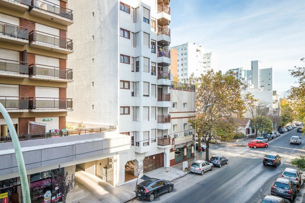 Edificio de varios pisos con balcones y autos estacionados en la calle
