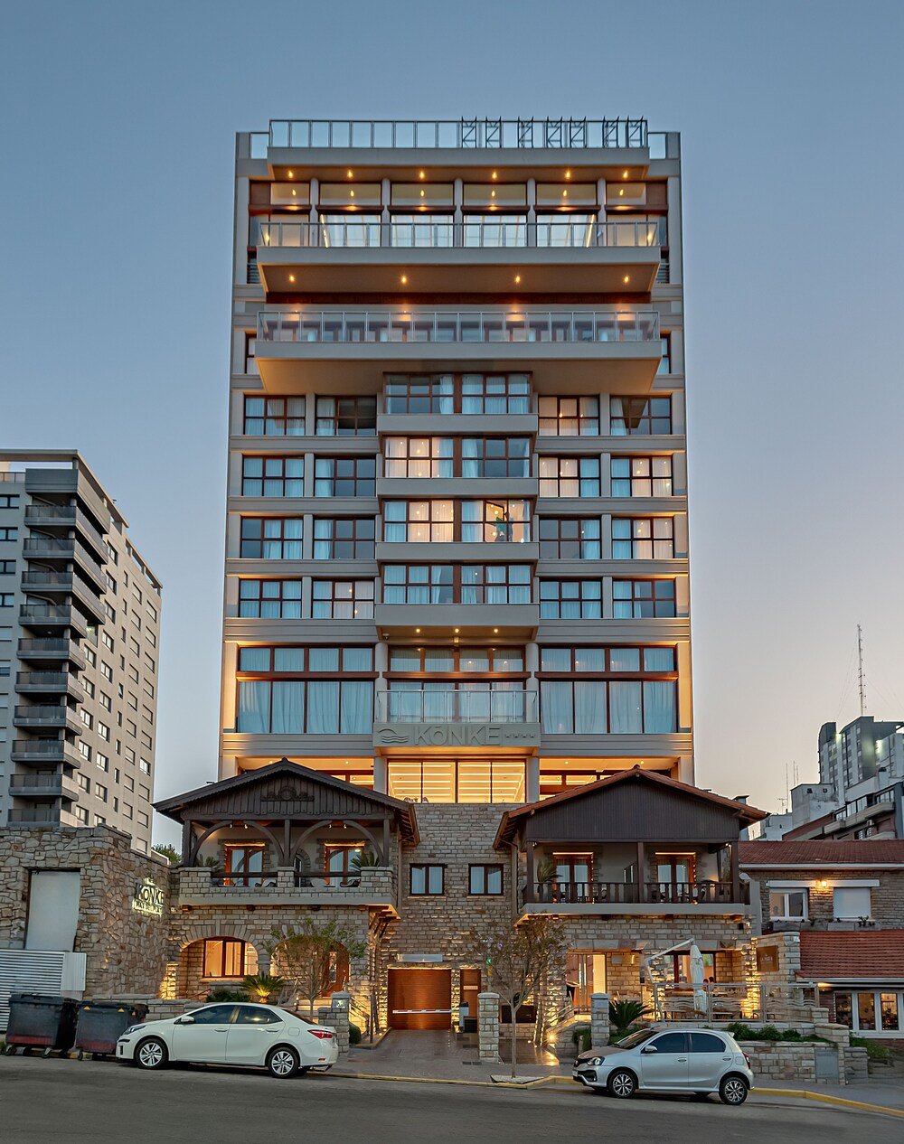 Fachada moderna del hotel con balcones, grandes ventanales y frente de piedra
