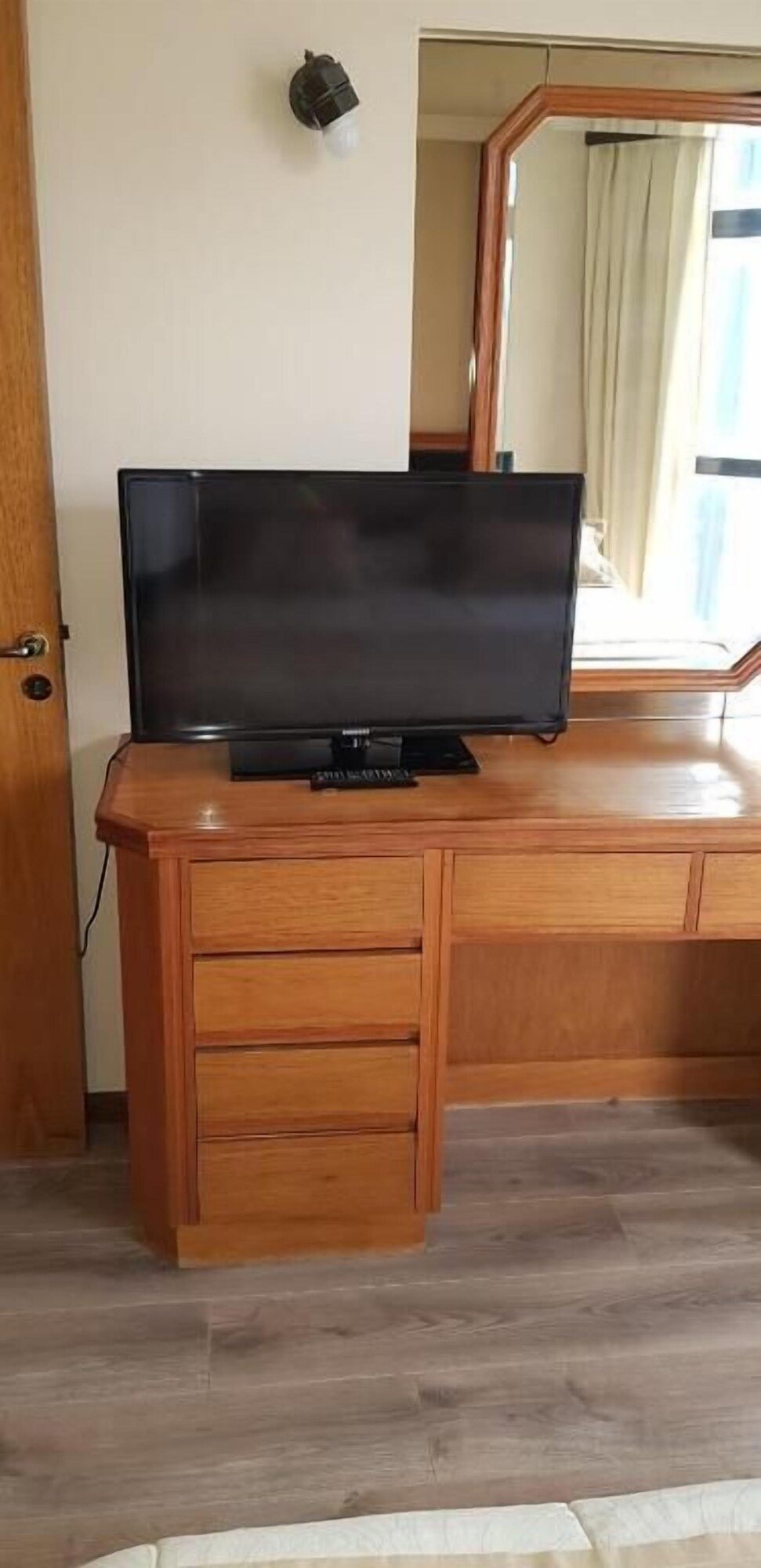 Escritorio de madera con televisor, espejo y puerta de la habitación