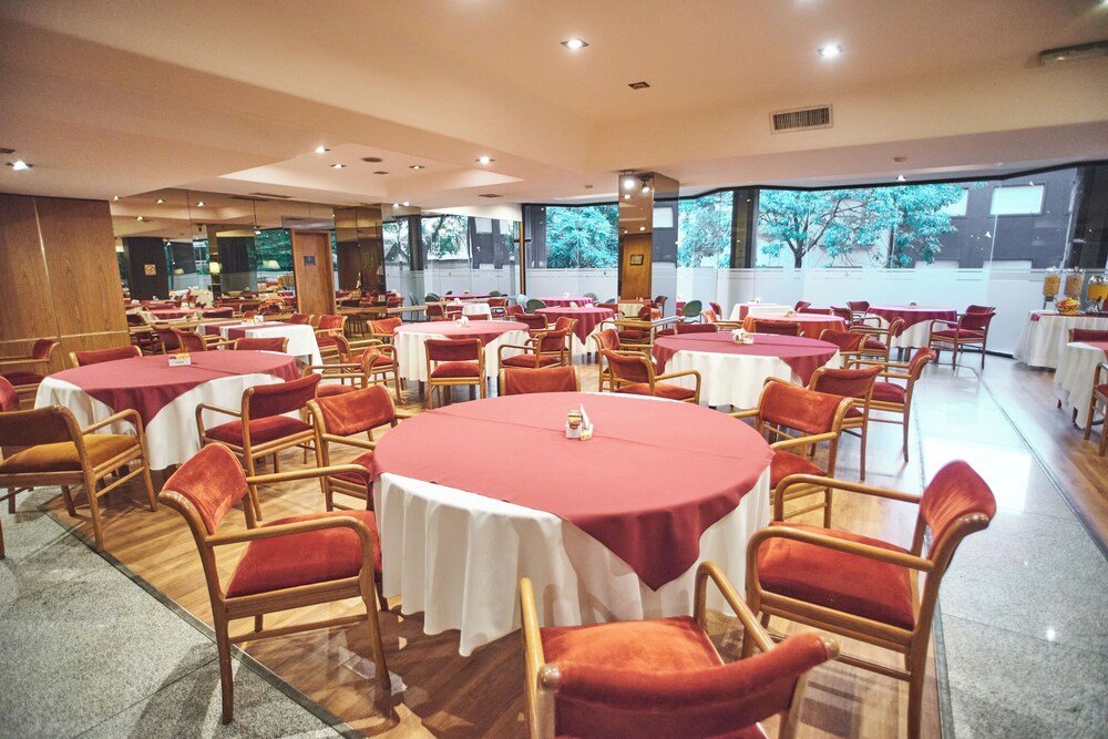 Comedor amplio con mesas redondas, sillas rojas y ventanales al verde