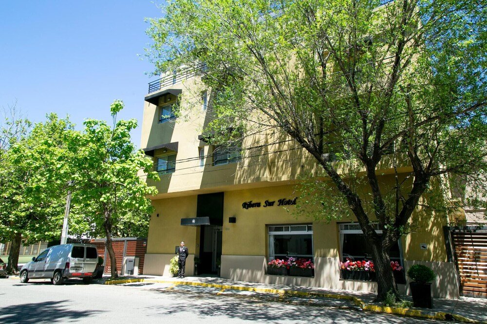 Fachada amarilla del hotel con balcón y jardineras en las ventanas