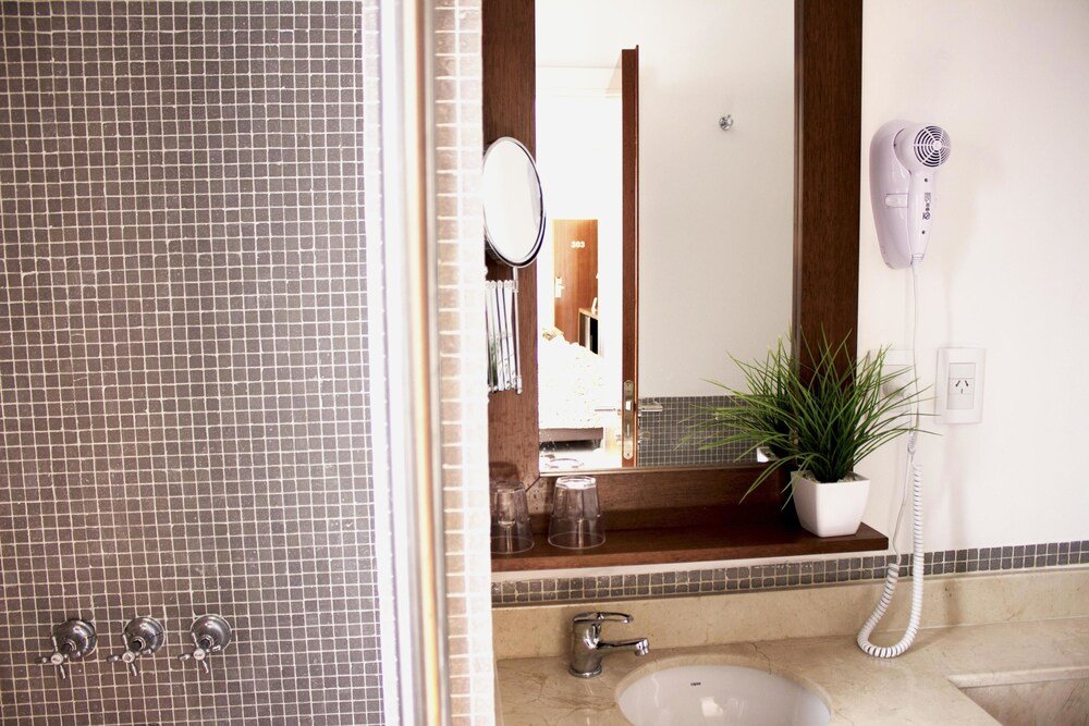 Baño con revestimiento, lavabo, espejo, secador y una planta