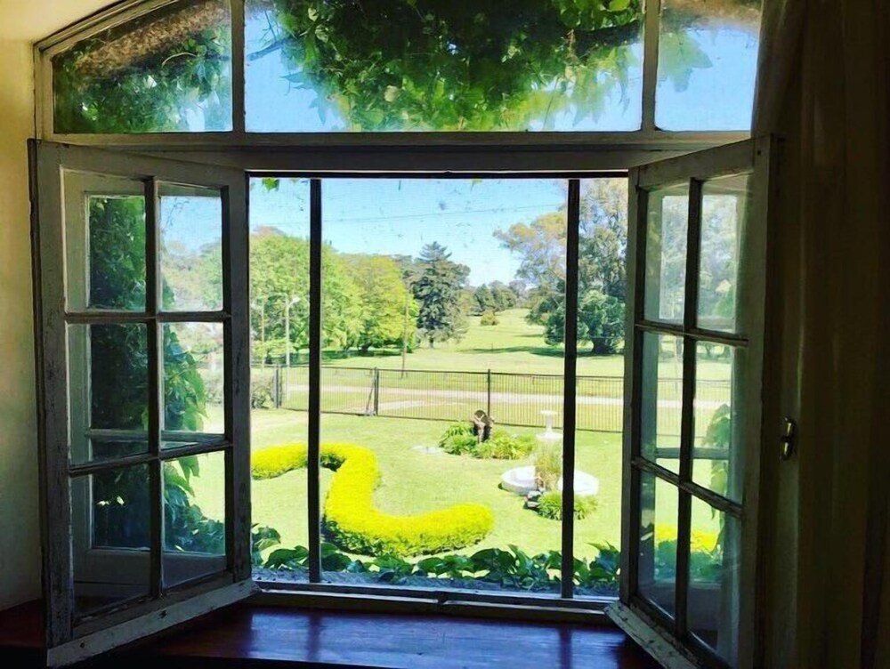 Habitación con gran ventana hacia un jardín cuidado con árboles