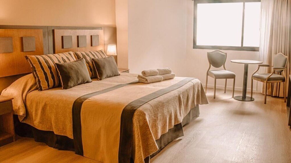 Habitación con cama grande, dos sillones, mesa y ventana