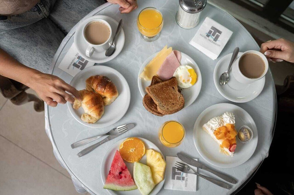 Desayuno servido con tostadas, huevos, jamón, frutas, café y jugo