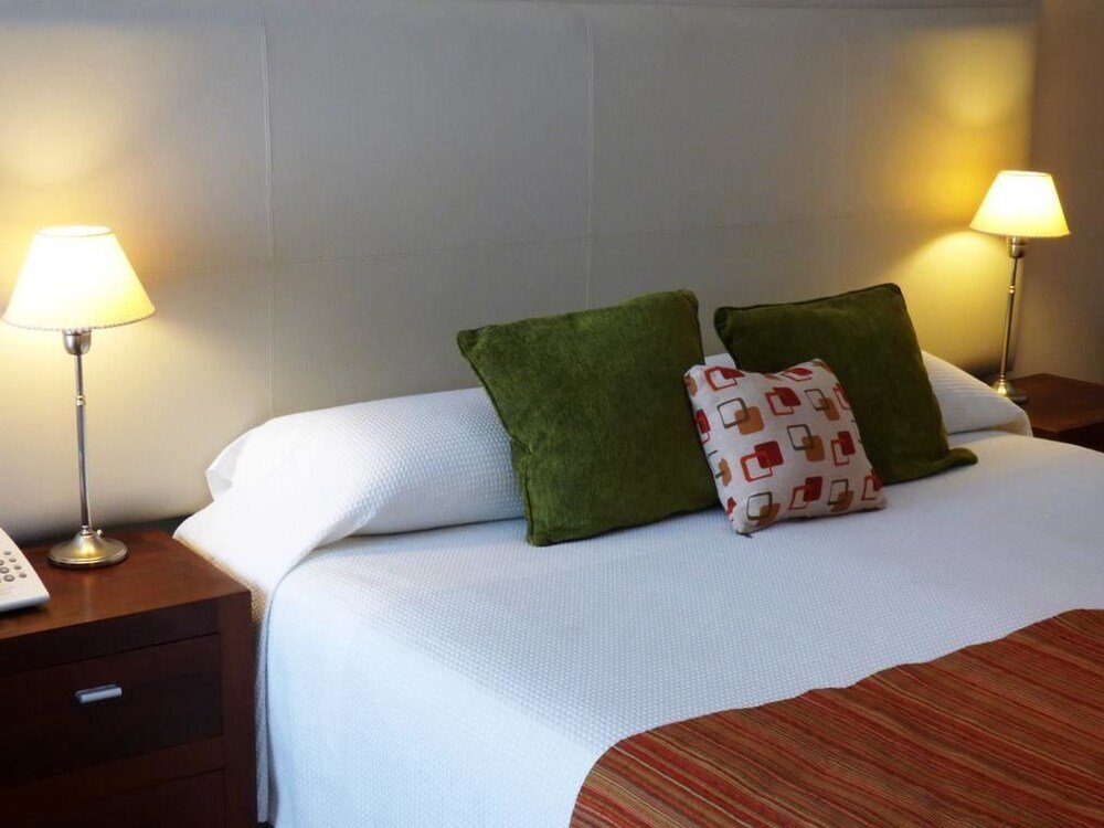 Cama bien tendida con sábanas blancas y almohadones verdes